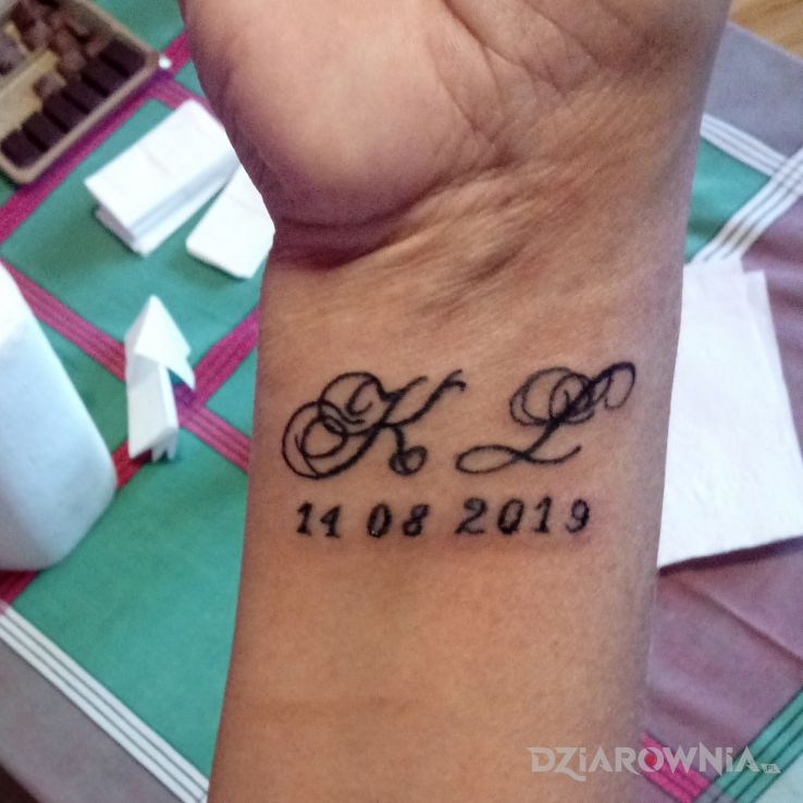 Tatuaż inicjaly z dats urodzenia w motywie napisy i stylu minimalistyczne na nadgarstku