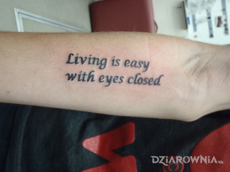 Tatuaż życie z zamkniętymi oczami w motywie napisy na przedramieniu