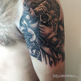Tatuaż Joker z aparatem na ramieniu motyw: czarno-szare styl: kreskówkowe / komiksowe