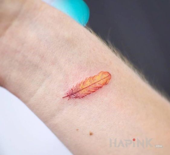 Tattoo Pomarańczowe piórko in colorful motif and handpoke style on the wrist