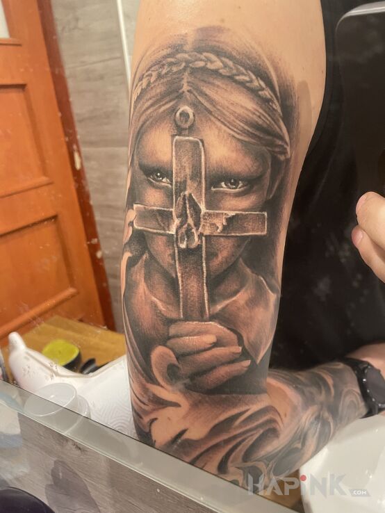 Tattoo Kobieta z krzyżem in religious motif and realistic style on the upper arm