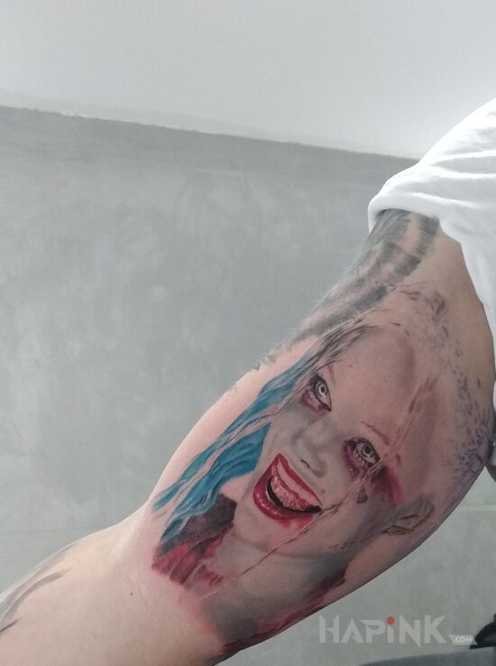 Tattoo Harley Quinn in colorful motif and realistic style on the upper arm