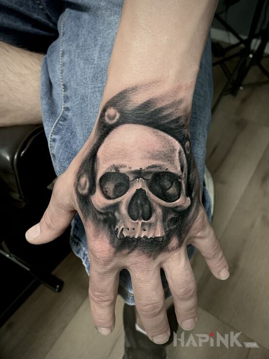 Tattoo S K U L L in black and gray motif and realistic style on the hand