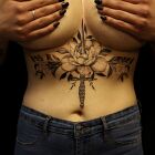 Tatuaż kwiatowa kompozycja i sztylet pod piersiami (underboob), motyw: ornamenty, styl: graficzne / ilustracyjne