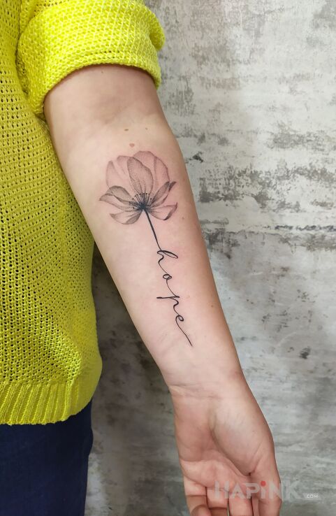 Tattoo Kwiat z napisem in black and gray motif and calligraphy style On the arm