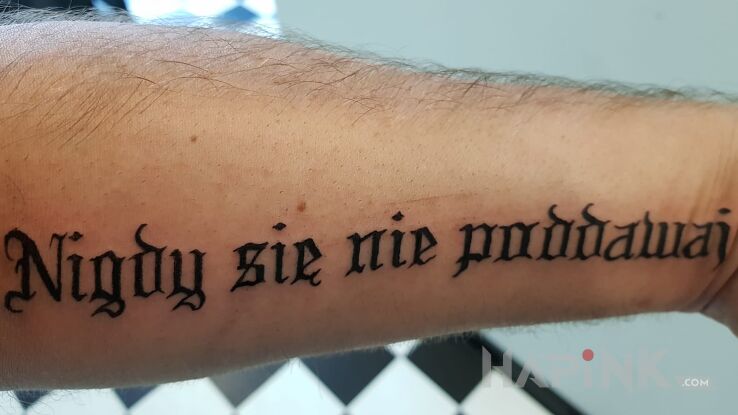 Tattoo Nigdy się nie poddawaj in lettering motif on the forearm