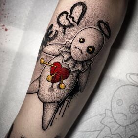 Tatuaż Laleczka Voodoo na przedramieniu motyw: czarno-szare styl: dotwork