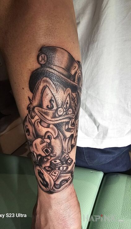 Tattoo Sknerus in black and gray motif and cartoon / comic book style on the forearm