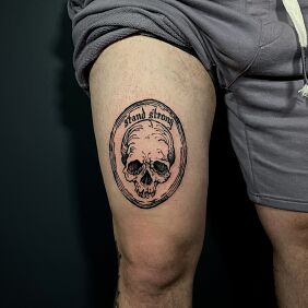 Tattoo Skull in a frame on the thigh motif: lettering style: engravings / gravure