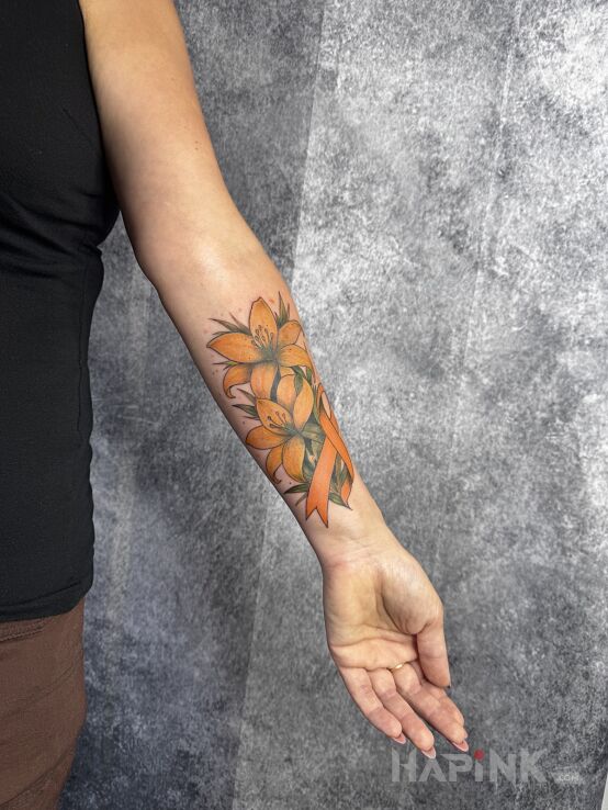 Tattoo Lilies with an orange ribbon in floral motif and graphic / illustrative style On the arm