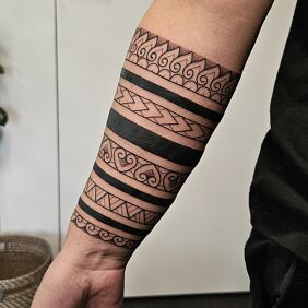 Tatuaż Czarne opaski przeplatane polinezyjskimi wzorami na ręce motyw: ornamenty styl: polinezyjskie