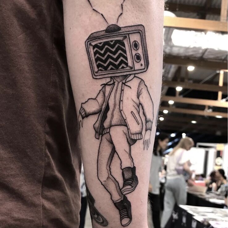 Tattoo Character with a TV instead of a head in objects motif and surrealistic style on the forearm