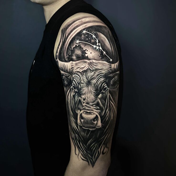 Tattoo Bull with a constellation above its head in black and gray motif and realistic style on the shoulder