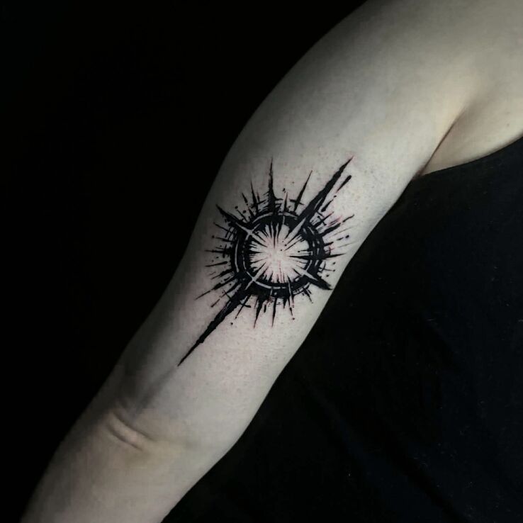 Tattoo Wheel with rays star in dark style in black and gray motif and blackwork / blackout style on the upper arm