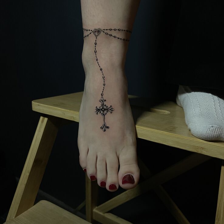 Tattoo Delicate Rosary in religious motif and realistic style on the foot
