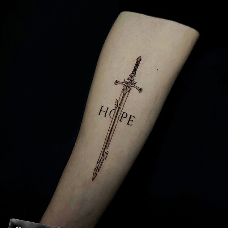 Tattoo Sword with the inscription HOPE in black and gray motif and graphic / illustrative style On the arm