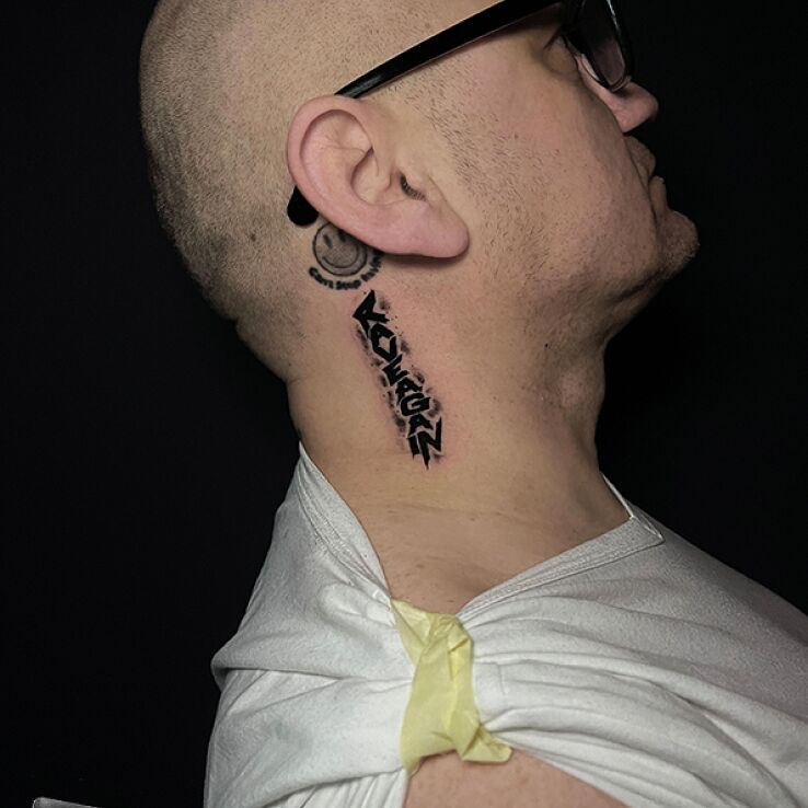 Tattoo Inscription "RAVEAGAIN" in black and gray motif and graphic / illustrative style behind the ear