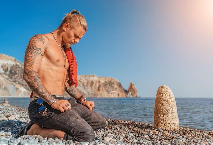 wytatuowany mężczyzna kucający na plaży