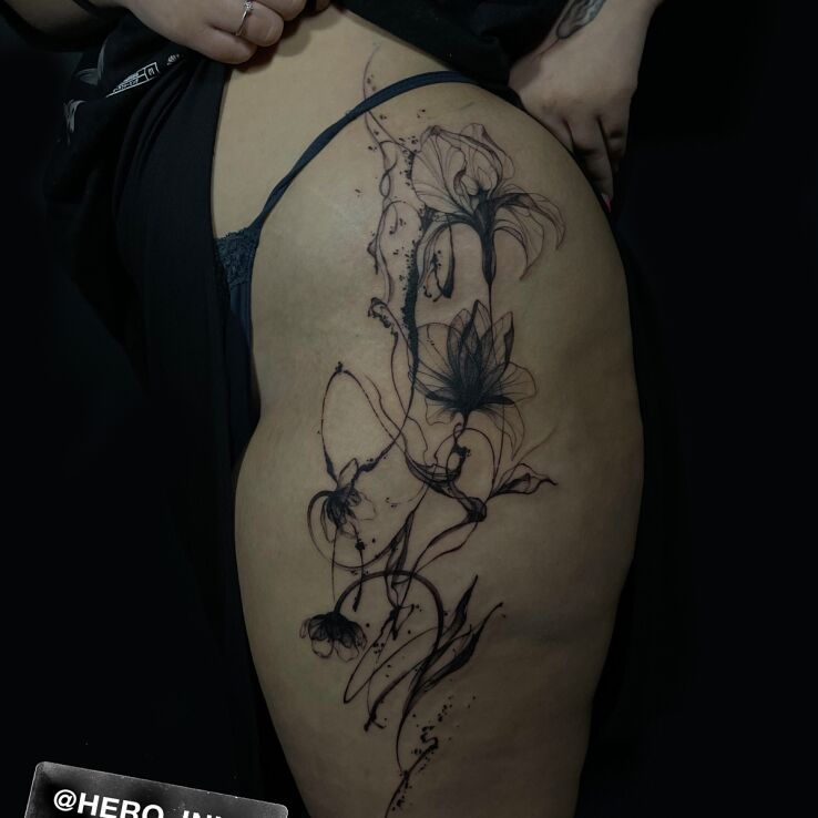 Tattoo Black flowers on the side of the thigh in flowers motif and blackwork / blackout style on the leg
