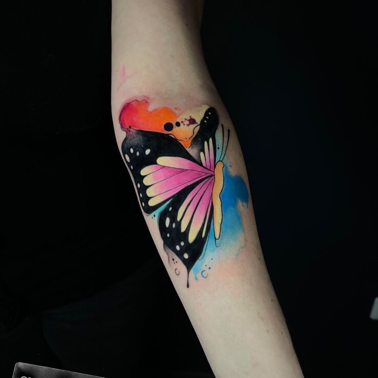 Tattoo Colorful butterfly with watercolor addition in colorful motif and graphic / illustrative style on the forearm