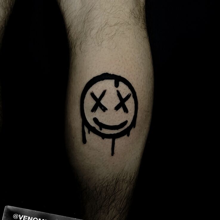 Tattoo Smiley face with X's in other motif and blackwork / blackout style on the leg