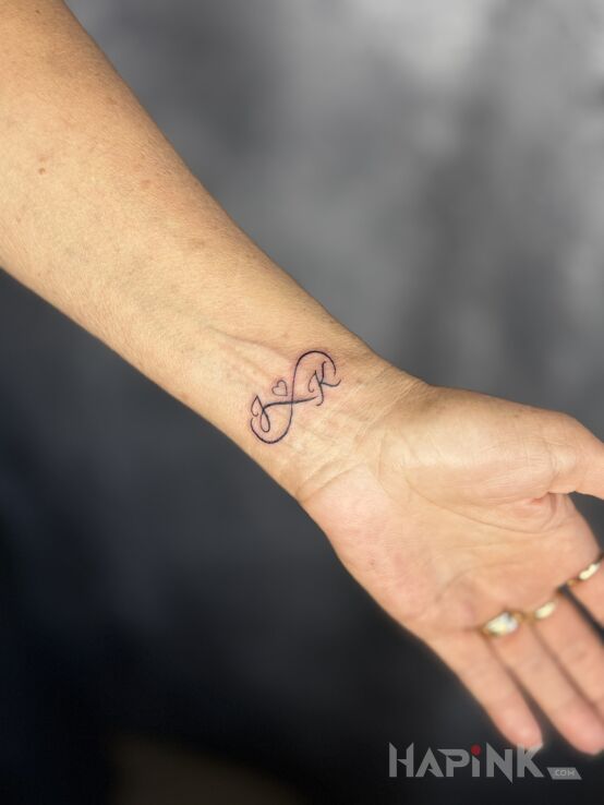 Tattoo Infinity with Letters in black and gray motif and minimalistic style On the arm