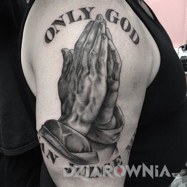 Tatuaż dłonie złożone do modlitwy i wytatuowany cytat na męskim ramieniu