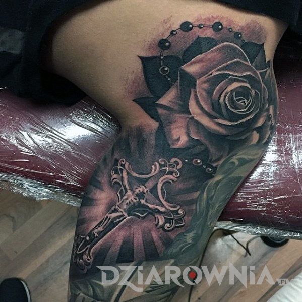 Tatuaż realistyczny przedstawiający różę i krzyż na nodze mężczyzny